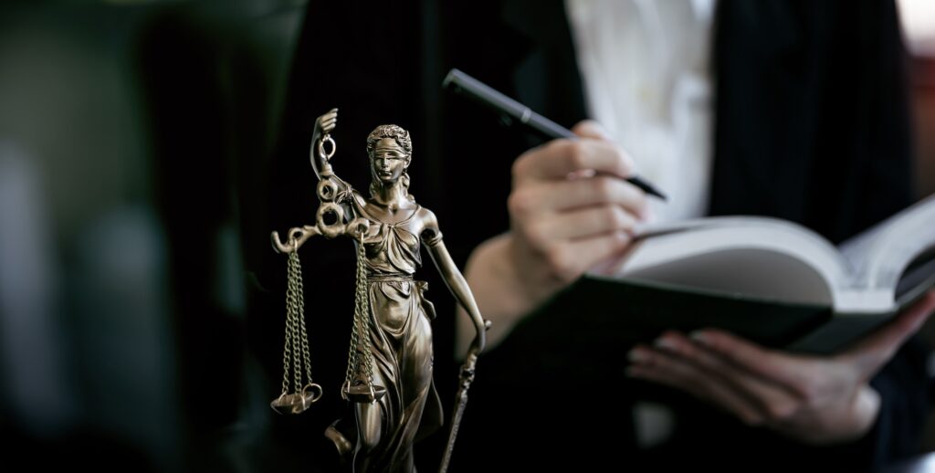 Estatua de la justicia en primer plano y profesional del derecho tomando notas al fondo.
